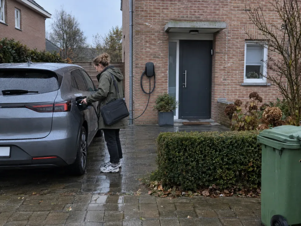 Vrouw koppelt 's ochtends haar elektrische wagen los van de laadpaal aan de gevel