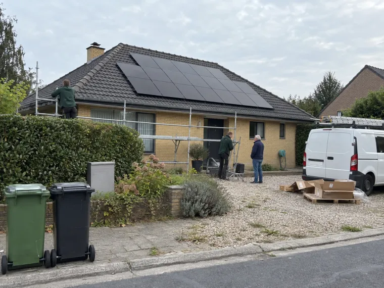 Monteurs breken de steiger af bij een bungalow met nieuwe zwarte zonnepanelen, terwijl de eigenaar met een van hen praat