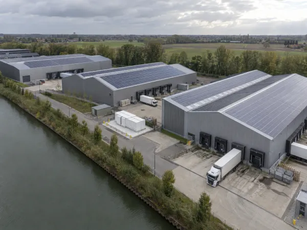 Luchtbeeld van bedrijfshallen met zonnepanelen langs een kanaal, met een batterijcontainer bij de laadkade