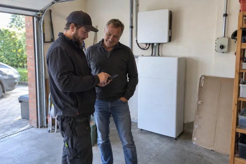 Installateur toont de eigenaar de energie-app, naast de nieuwe thuisbatterij in de garage