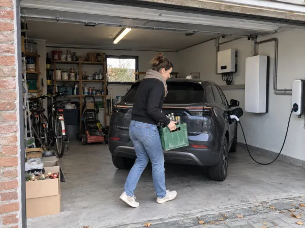 Open garage met een thuisbatterij en omvormer aan de muur en een elektrische wagen aan de laadpaal