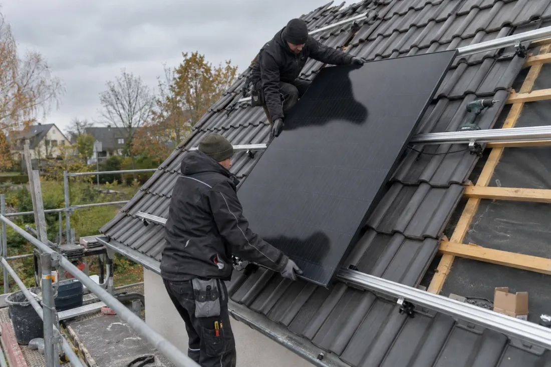 Twee monteurs leggen een zwart zonnepaneel op de montagerails van een pannendak