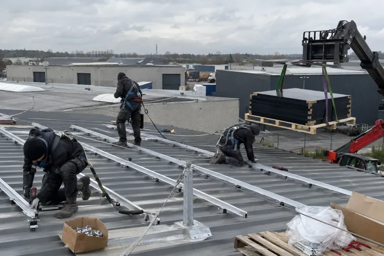 Monteurs met valbeveiliging plaatsen montagerails op het dak van een bedrijfshal