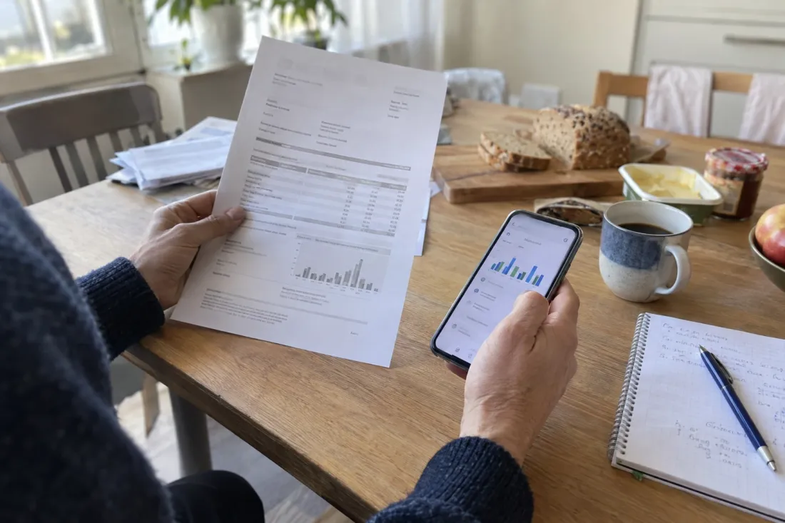 De jaarafrekening naast de energie-app op een smartphone, aan de keukentafel