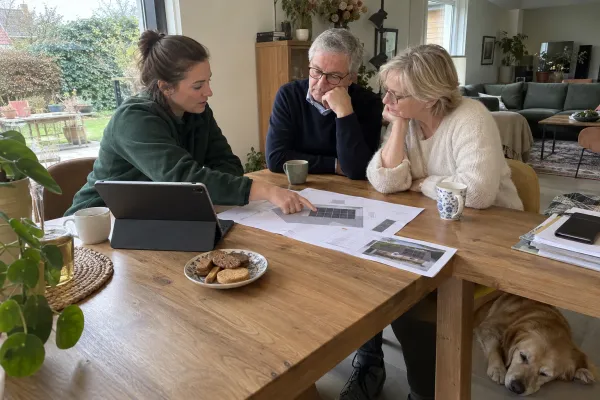 Energieadviseur overloopt aan de eettafel het dakplan met de zonnepanelen samen met een koppel